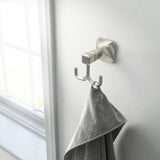 Silver double hook with a gray towel on a white wall.